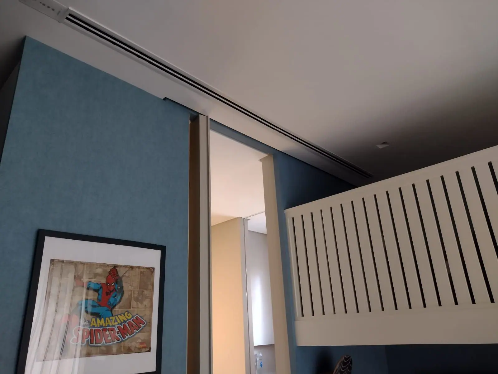 Long linear diffuser along a white ceiling above a blue wall, a sliding door and a slatted railing