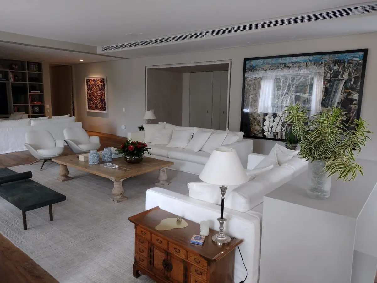 Long linear diffuser set into the ceiling above a large living room with white sofas and framed artwork