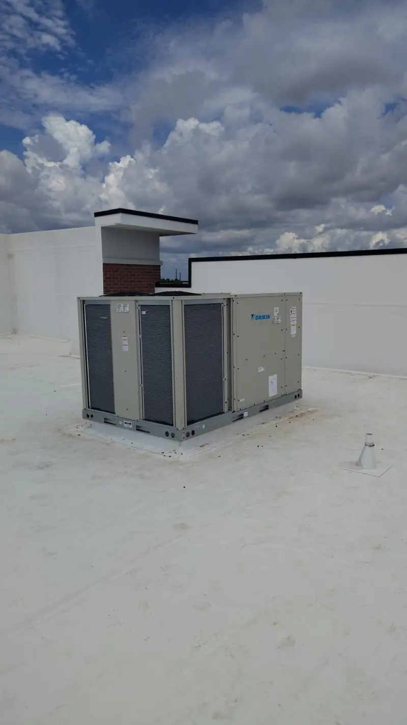 Rooftop package unit on a flat white roof under a partly cloudy sky